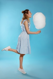 Full length portrait of pretty young woman with tasty cotton candy on blue background