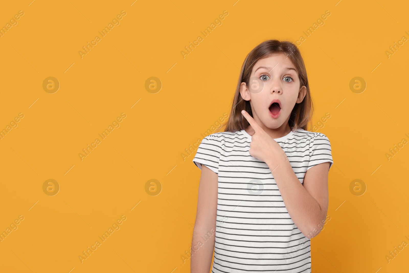 Photo of Surprised girl pointing at something on yellow background. Space for text