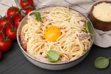 Photo of Bowl of tasty pasta Carbonara with basil leaves and egg yolk on grey wooden table