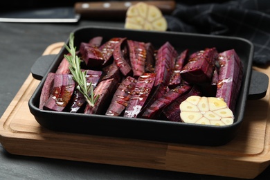 Photo of Black raw cut carrot with garlic and rosemary in baking dish on black table, closeup