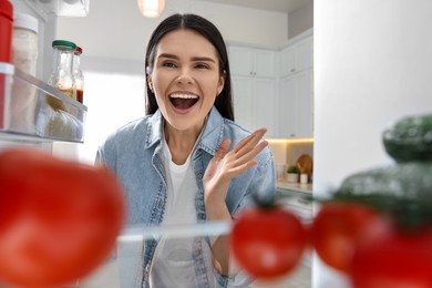 Photo of Excited woman near refrigerator in kitchen, view from inside