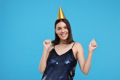Photo of Happy young woman in party hat dancing on light blue background