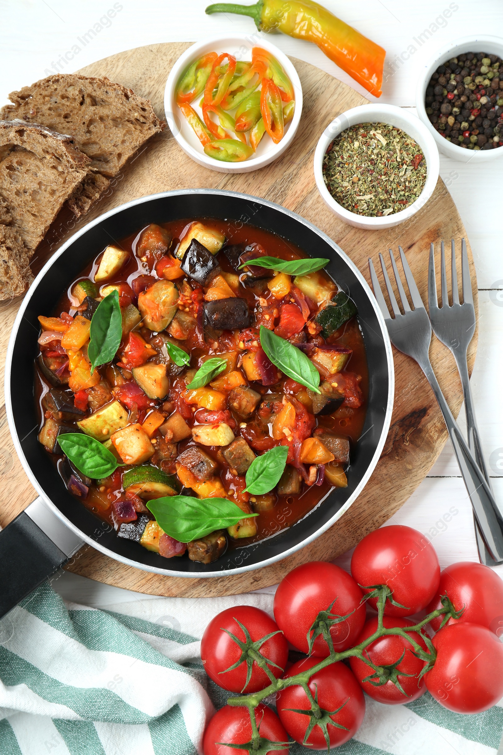 Photo of Frying pan with tasty ratatouille, ingredients and bread on white wooden table, flat lay