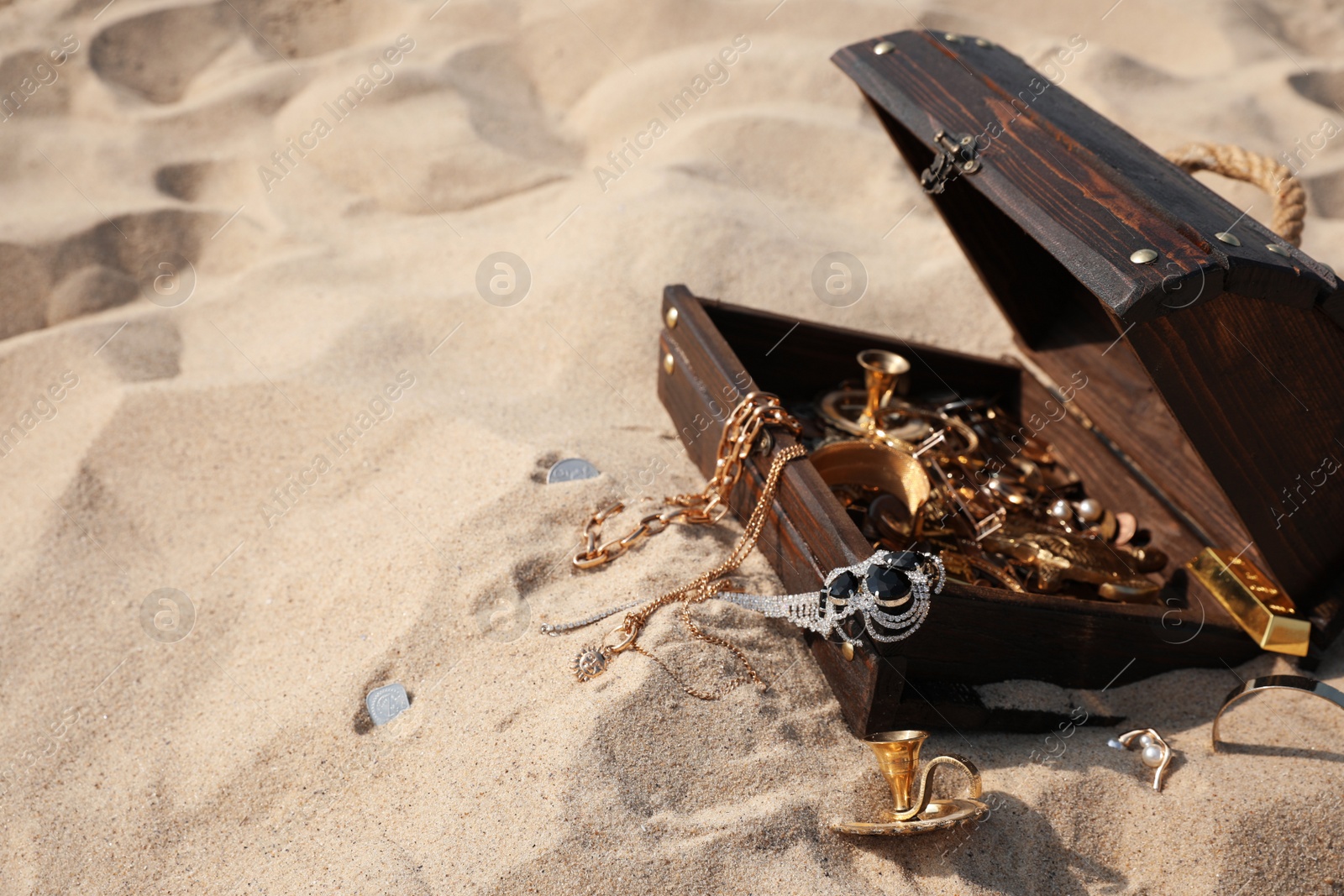 Photo of Open wooden treasure chest on sand, space for text