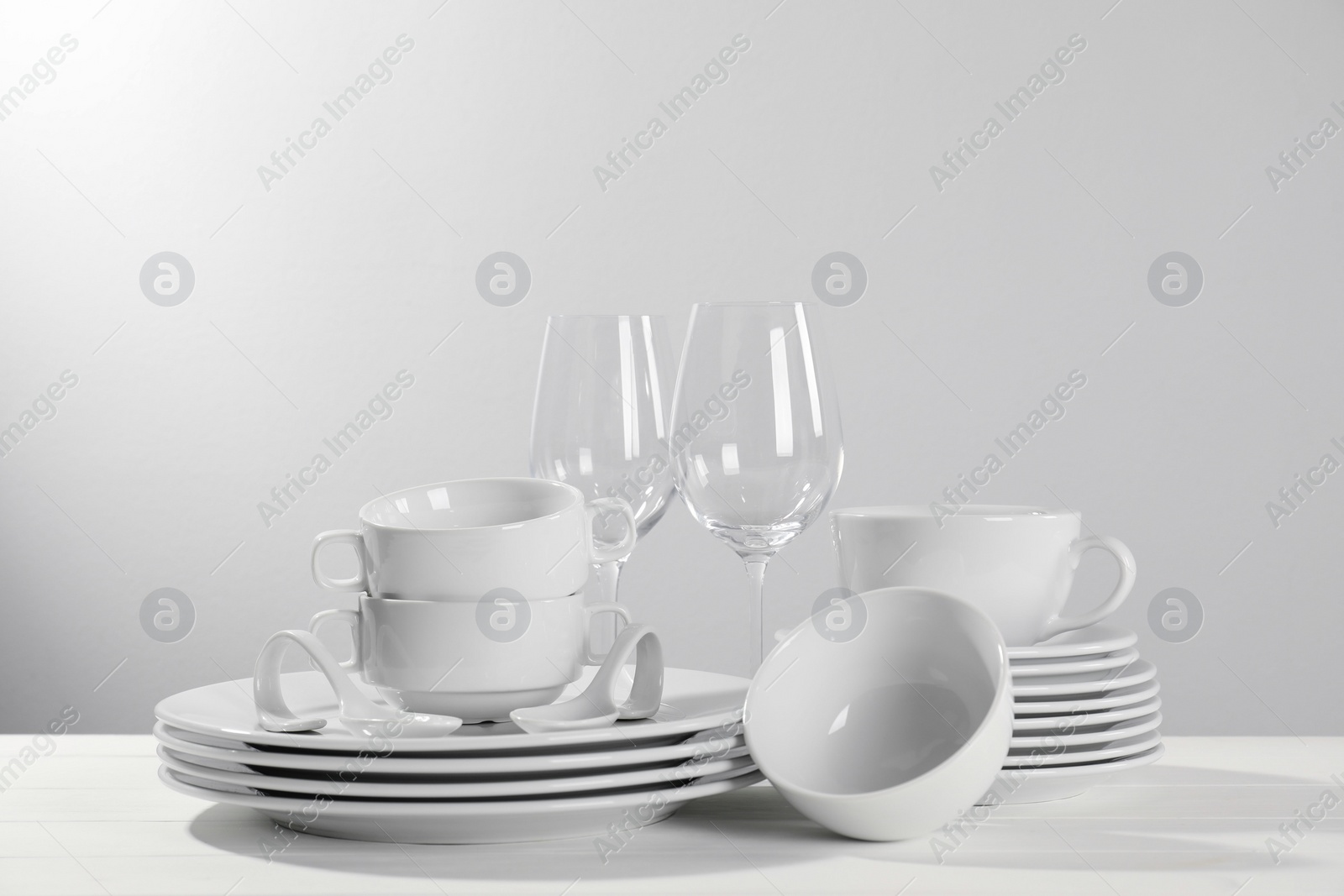 Photo of Set of clean dishware and glasses on white wooden table against light background