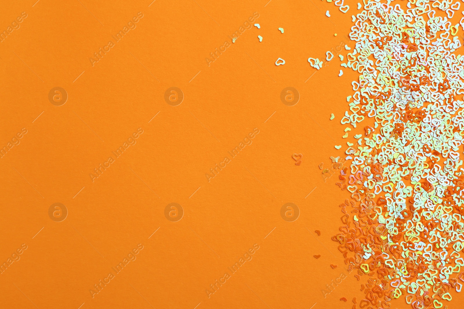 Photo of Shiny bright heart shaped glitter on orange background, top view. Space for text