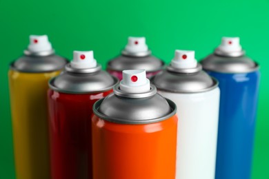 Photo of Colorful cans of spray paints on green background, closeup
