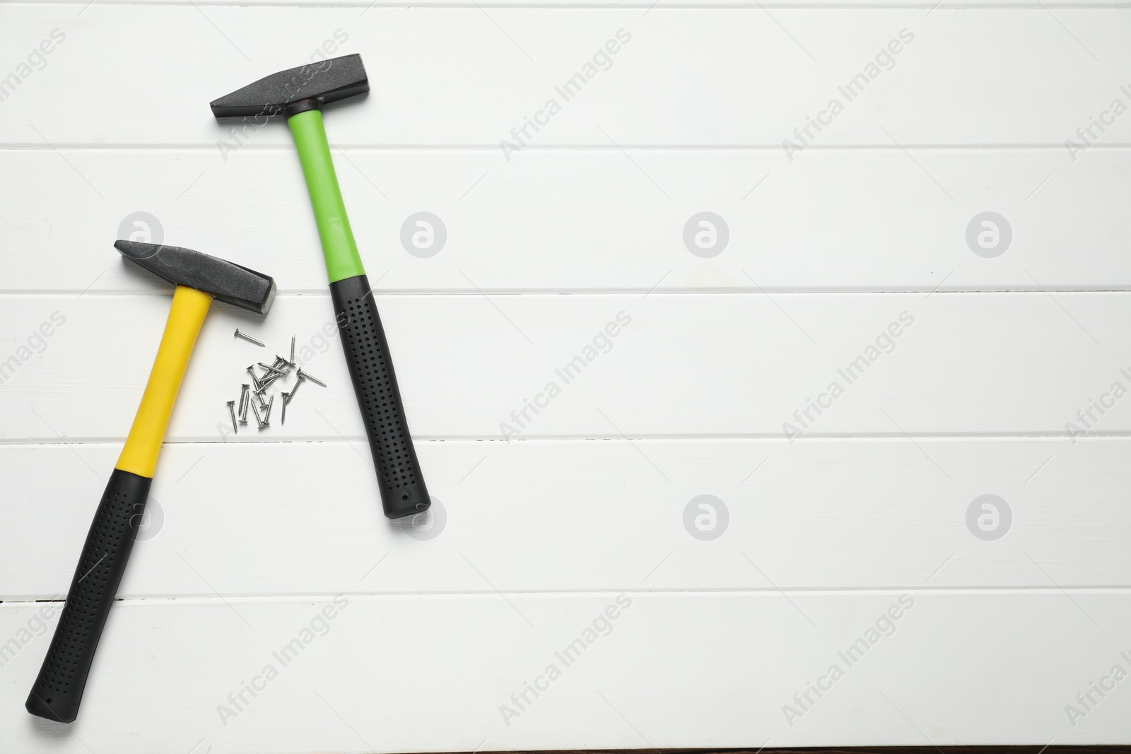 Photo of Hammers and metal nails on white wooden table, flat lay. Space for text