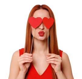 Young woman in red dress covering her eyes with paper hearts on white background