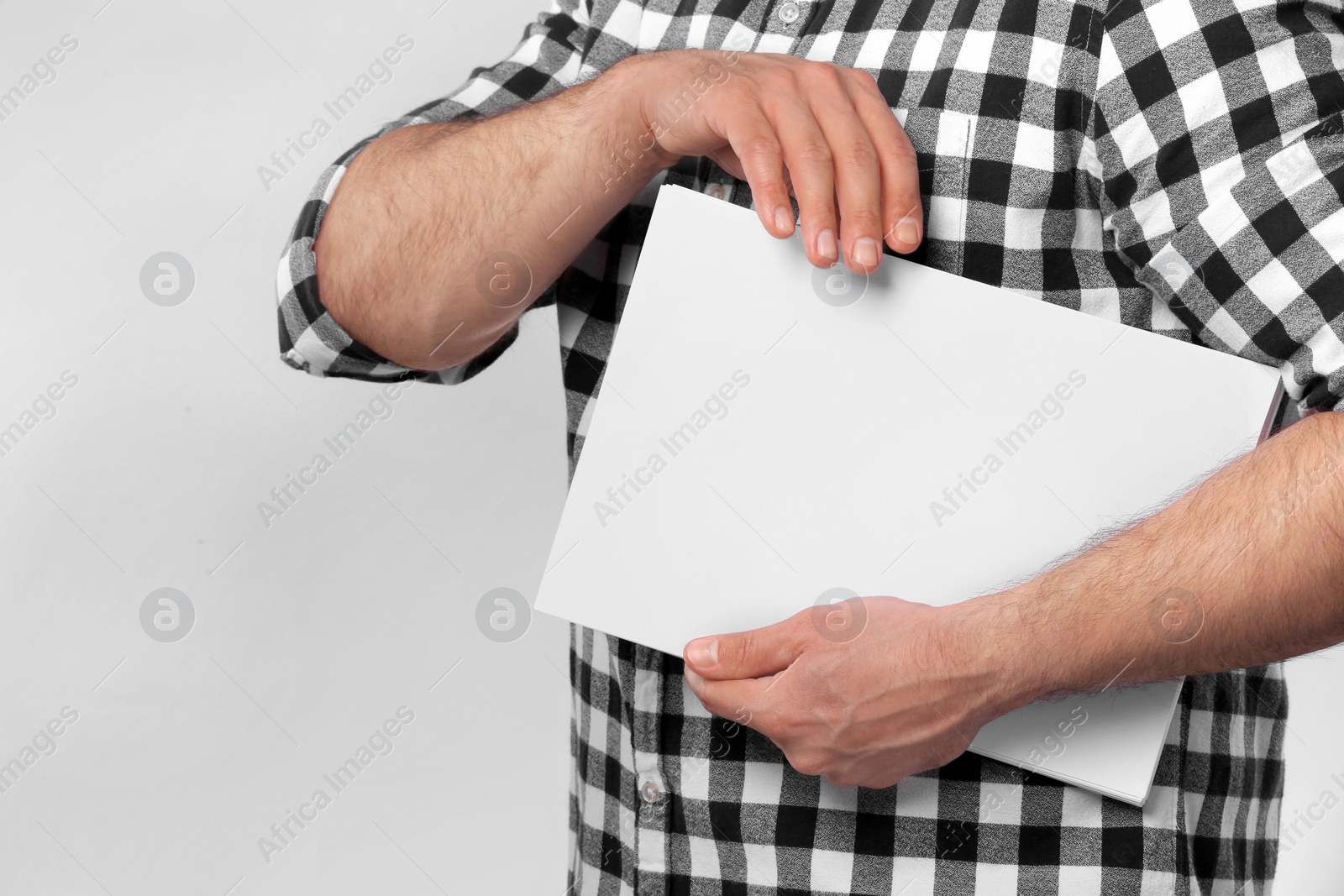 Photo of Man holding sheet of paper on light grey background, closeup. Mockup for design