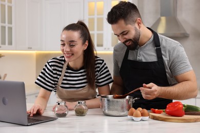 Photo of Happy lovely couple using laptop while cooking in kitchen