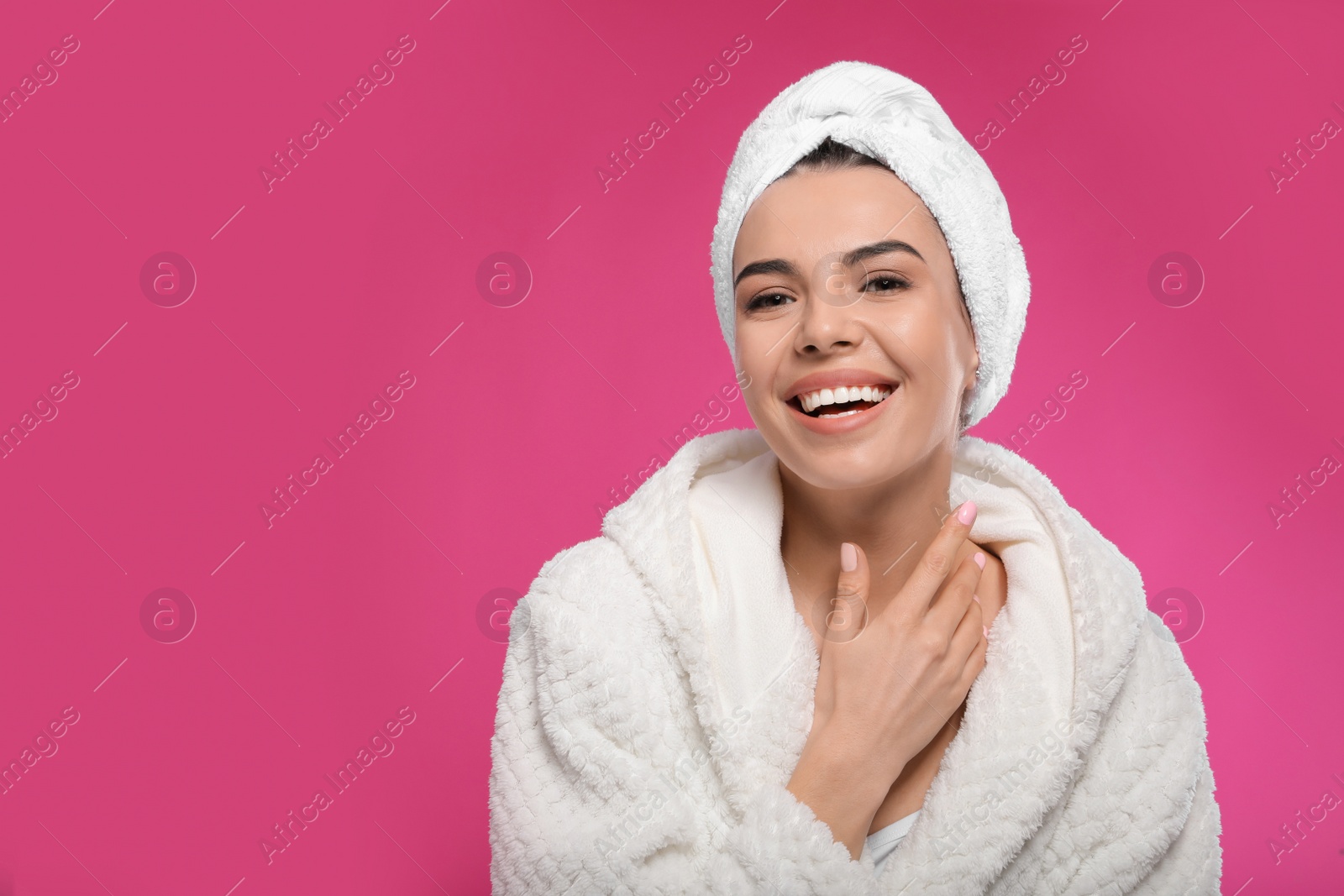 Photo of Happy young woman in bathrobe with towel on head against pink background, space for text. Washing hair