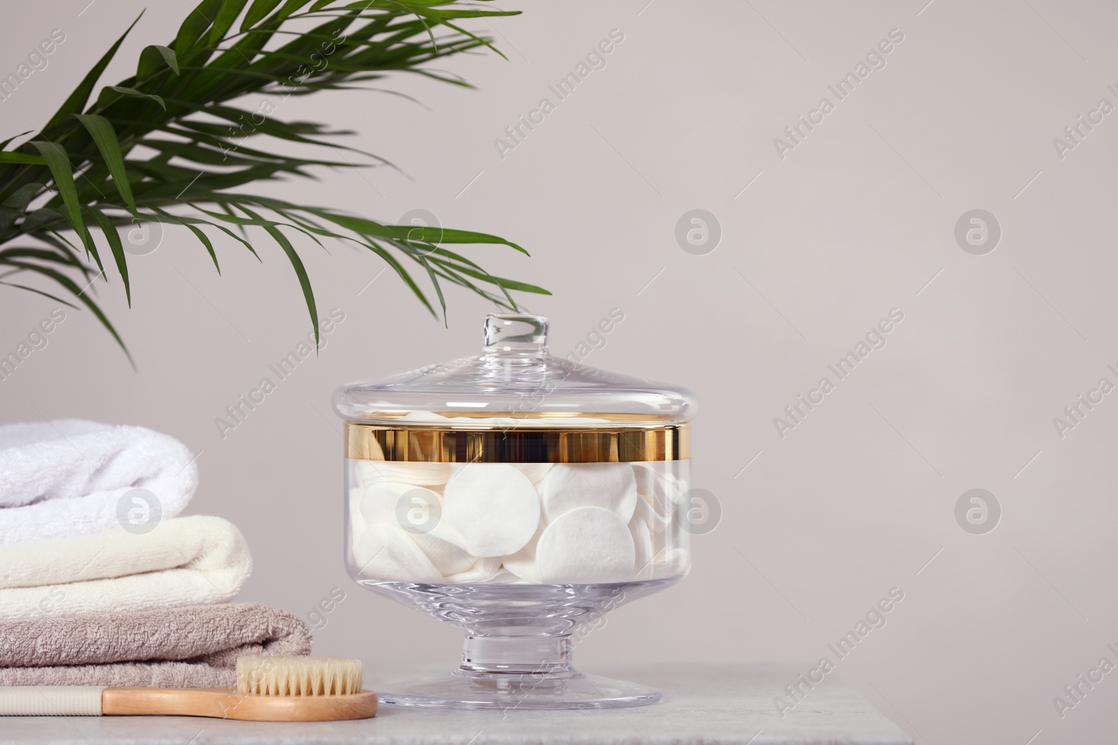 Photo of Composition of glass jar with cotton pads on table near light wall. Space for text