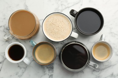 Different coffee drinks in cups on white marble table, flat lay