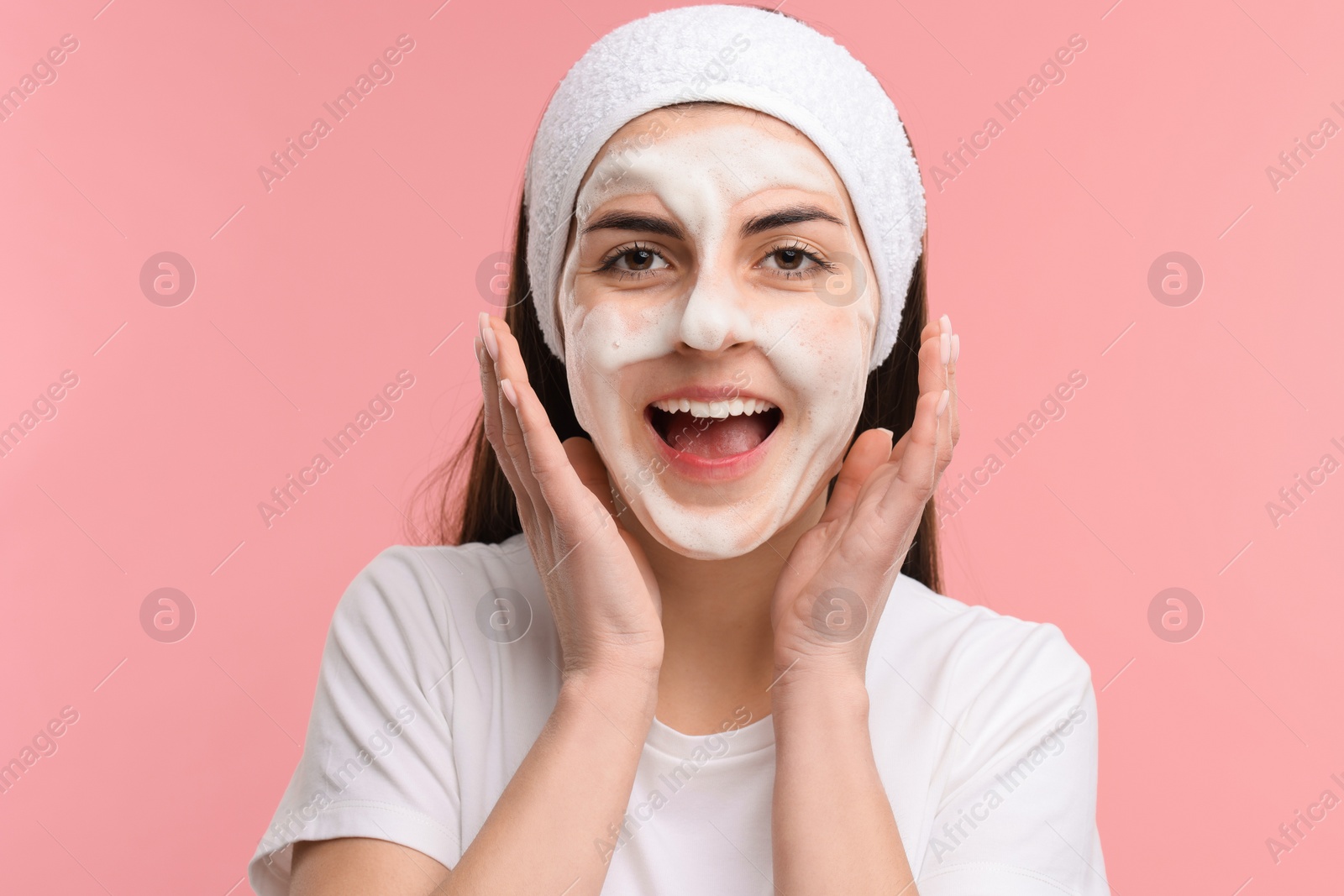 Photo of Young woman with headband washing her face on pink background