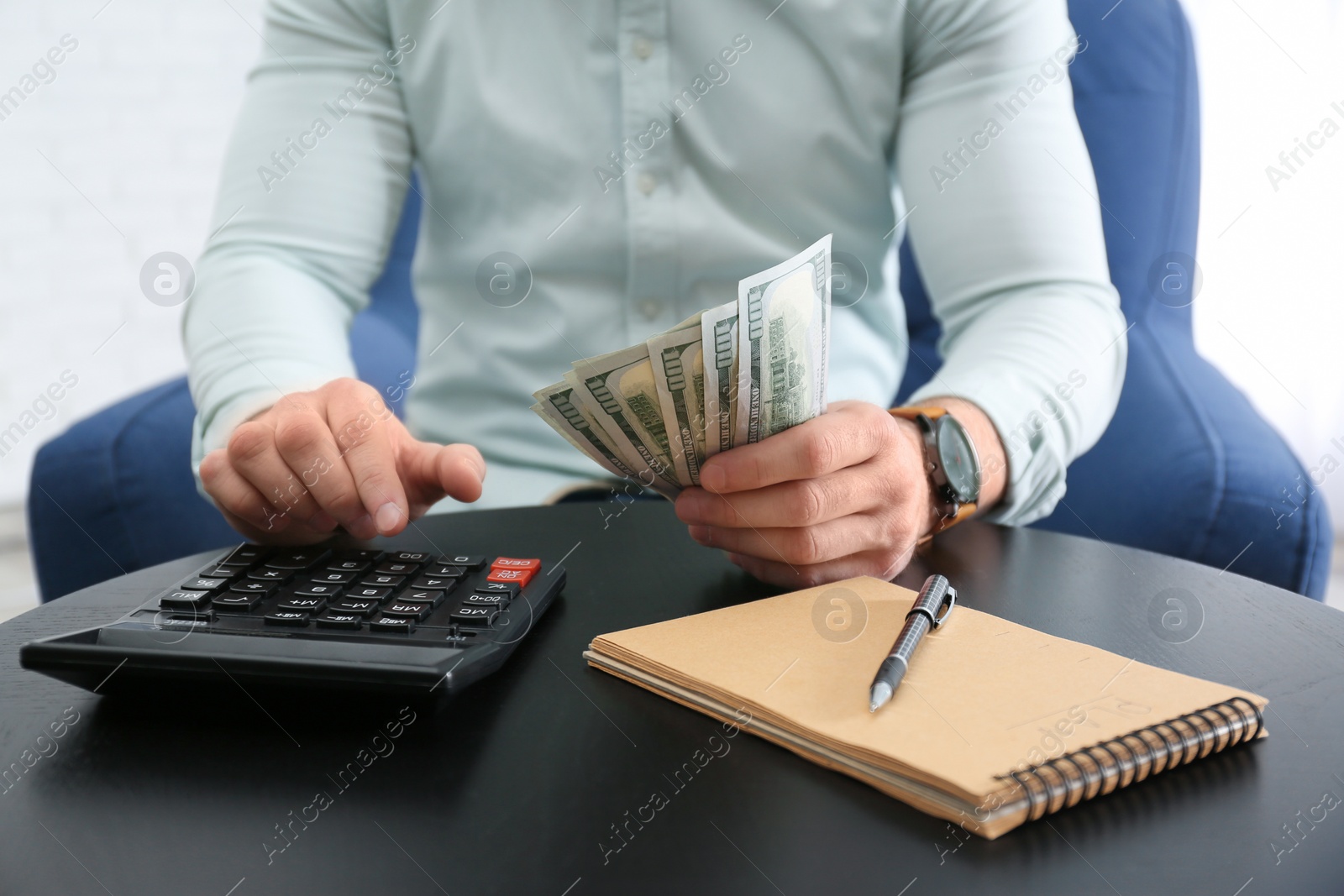 Photo of Businessman with money, calculator and notebook at table against light background, closeup