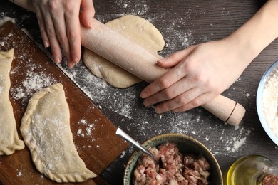 Woman rolling dough for chebureki at wooden table, top view