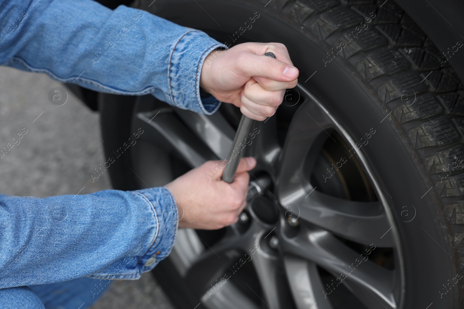 Photo of Young man changing tire of car on roadside, closeup