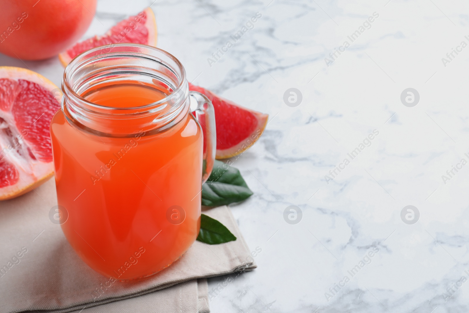 Photo of Tasty freshly made grapefruit juice on white marble table. Space for text