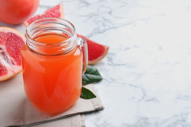 Photo of Tasty freshly made grapefruit juice on white marble table. Space for text