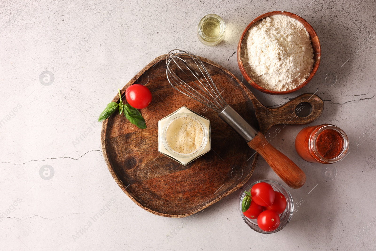Photo of Pizza dough starter in glass jar, products and whisk on gray textured table, flat lay