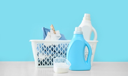 Detergents and children's clothes on white table near light blue wall. Space for text