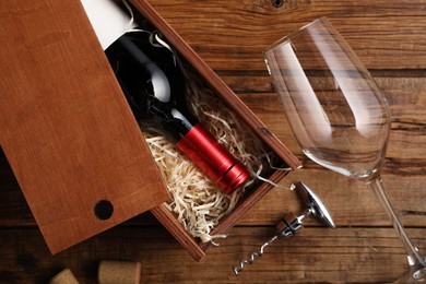 Box with wine bottle, glass, corkscrew and corks on wooden table, flat lay