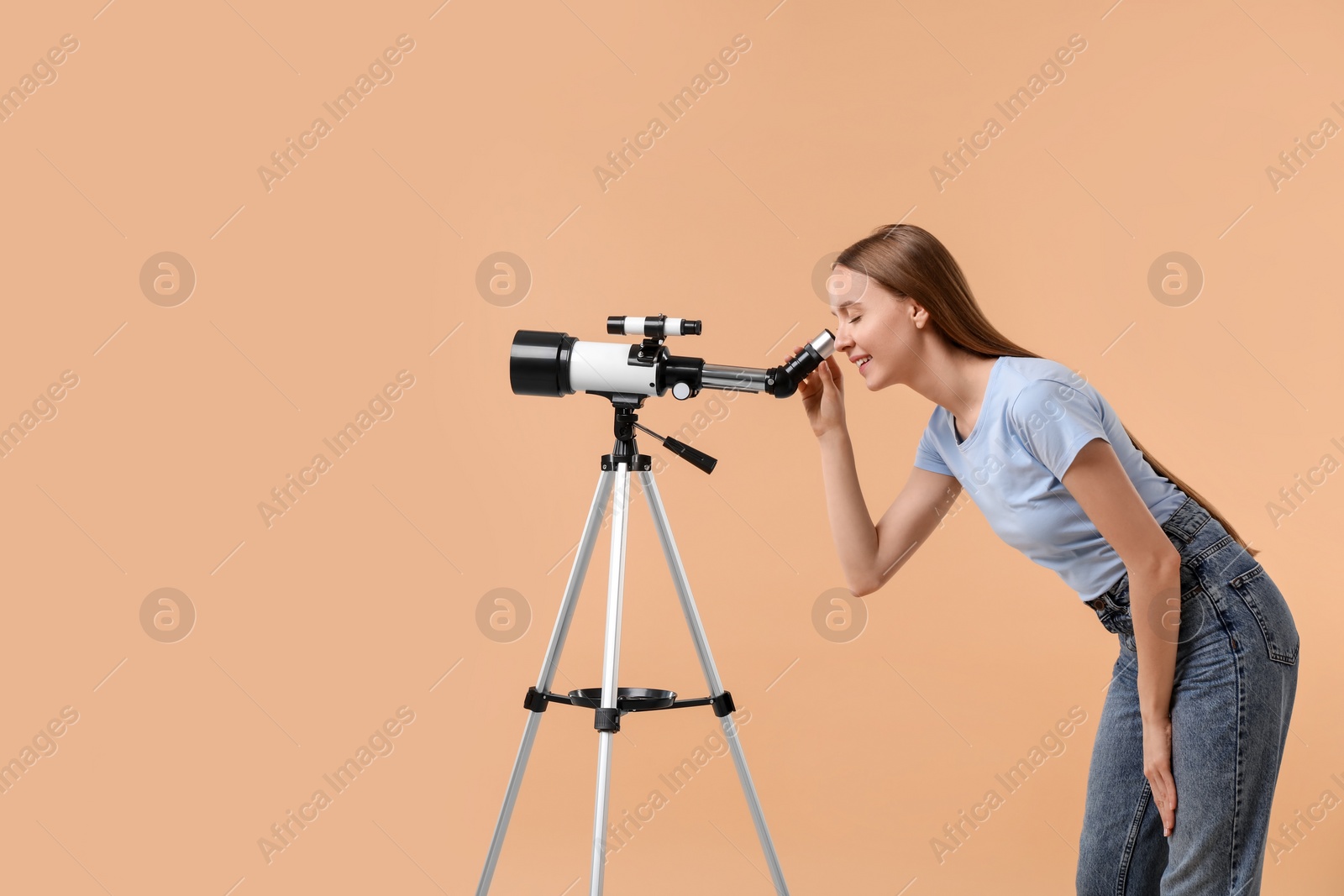 Photo of Young astronomer looking at stars through telescope on beige background, space for text