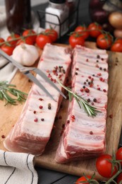Photo of Raw pork ribs with peppercorns and rosemary on table, closeup