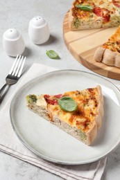 Photo of Tasty quiche with chicken, vegetables, basil and cheese served on light table