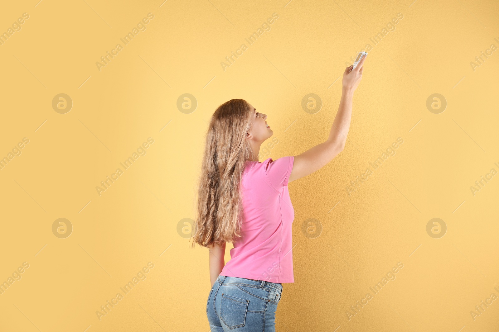 Photo of Young woman with air conditioner remote on color background