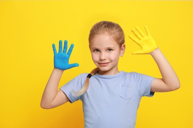 Photo of Little girl with hands painted in Ukrainian flag colors on yellow background. Love Ukraine concept