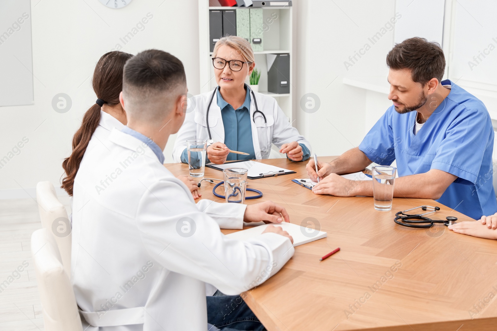 Photo of Medical conference. Team of doctors listening to speaker at wooden table in clinic