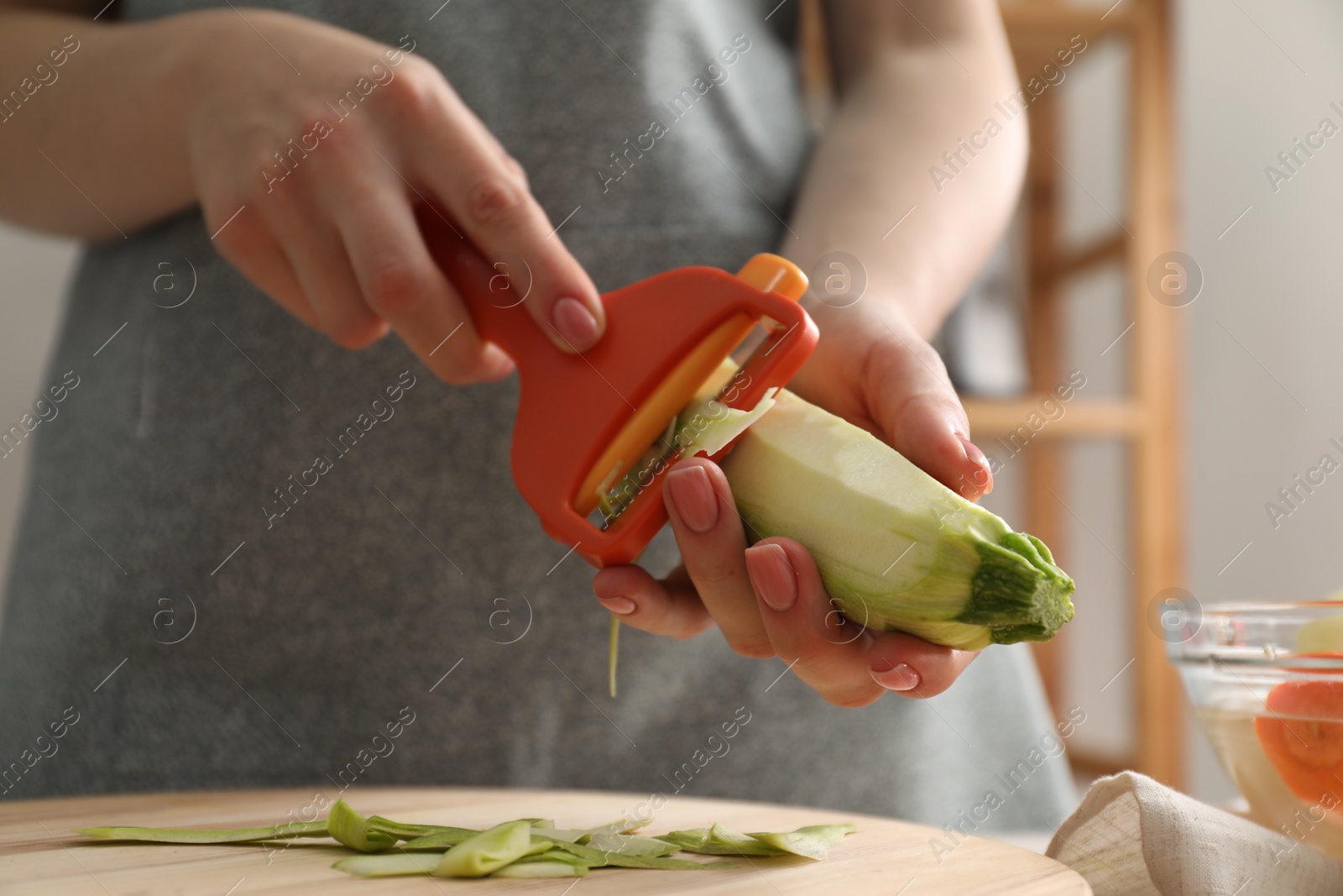 Photo of Woman peeling fresh zucchini at table indoors, closeup