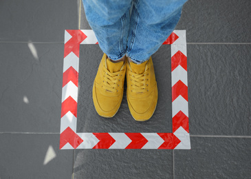 Photo of Woman standing on taped floor marking for social distance, top view. Coronavirus pandemic