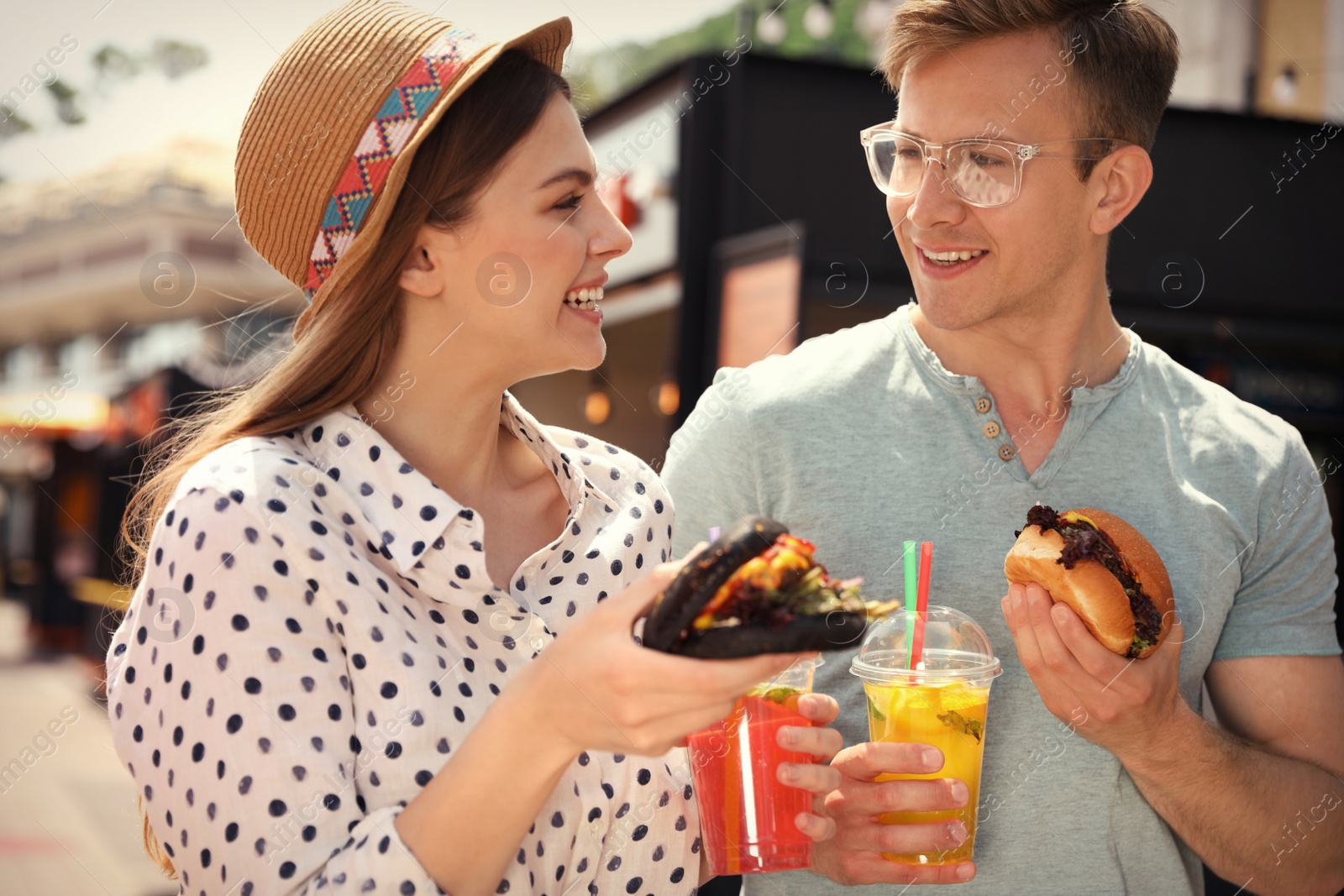 Photo of Young happy couple with burgers walking on city street