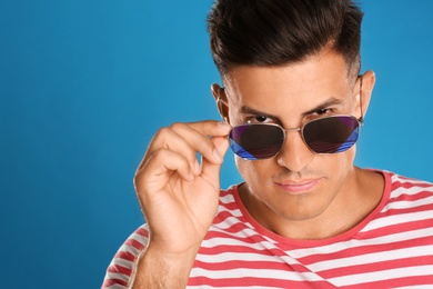 Photo of Handsome man wearing sunglasses on blue background, closeup