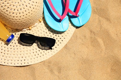Straw hat, sunglasses, flip flops and refreshing drink on sand, flat lay with space for text. Beach accessories