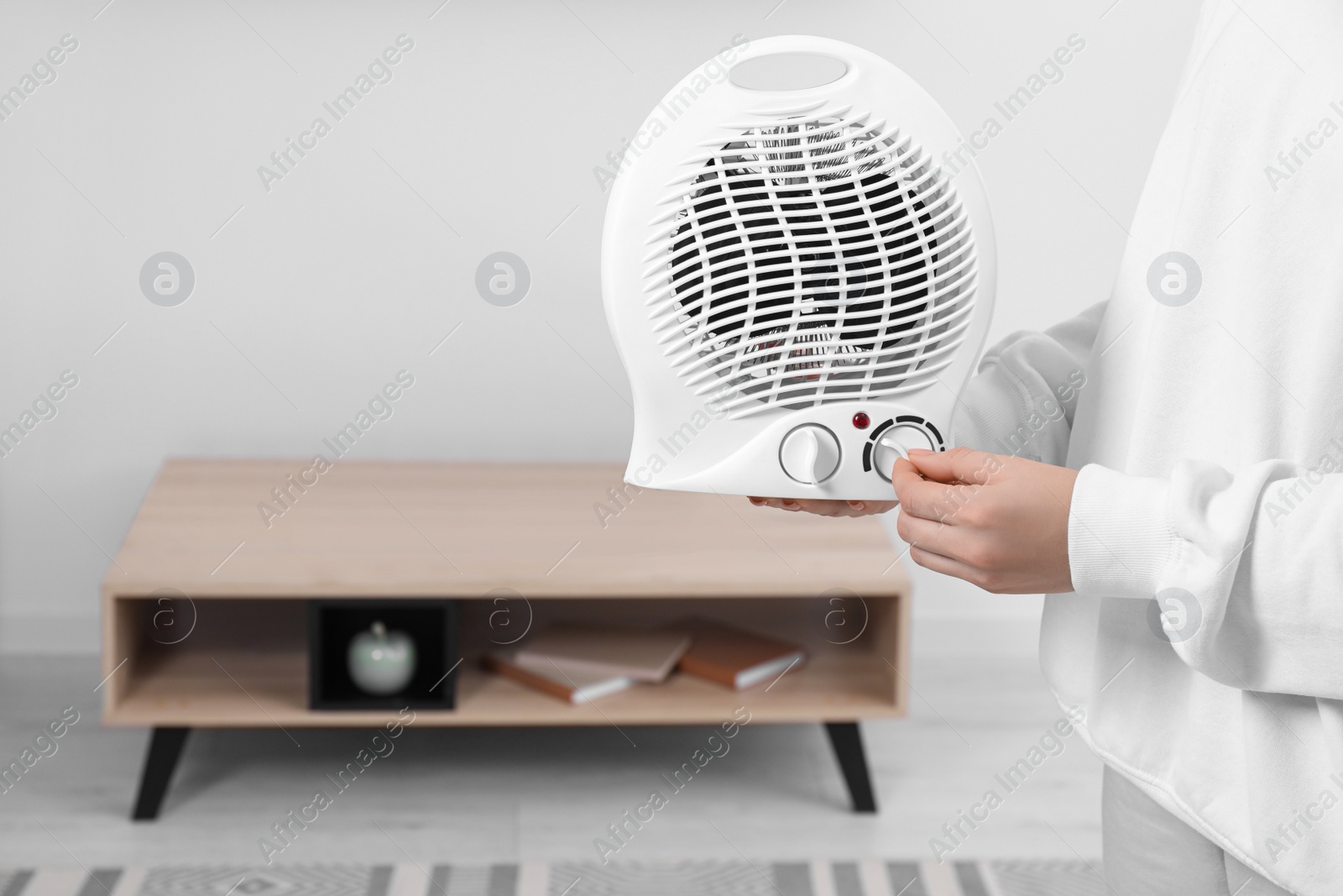 Photo of Woman turning on electric fan heater at home, closeup. Space for text