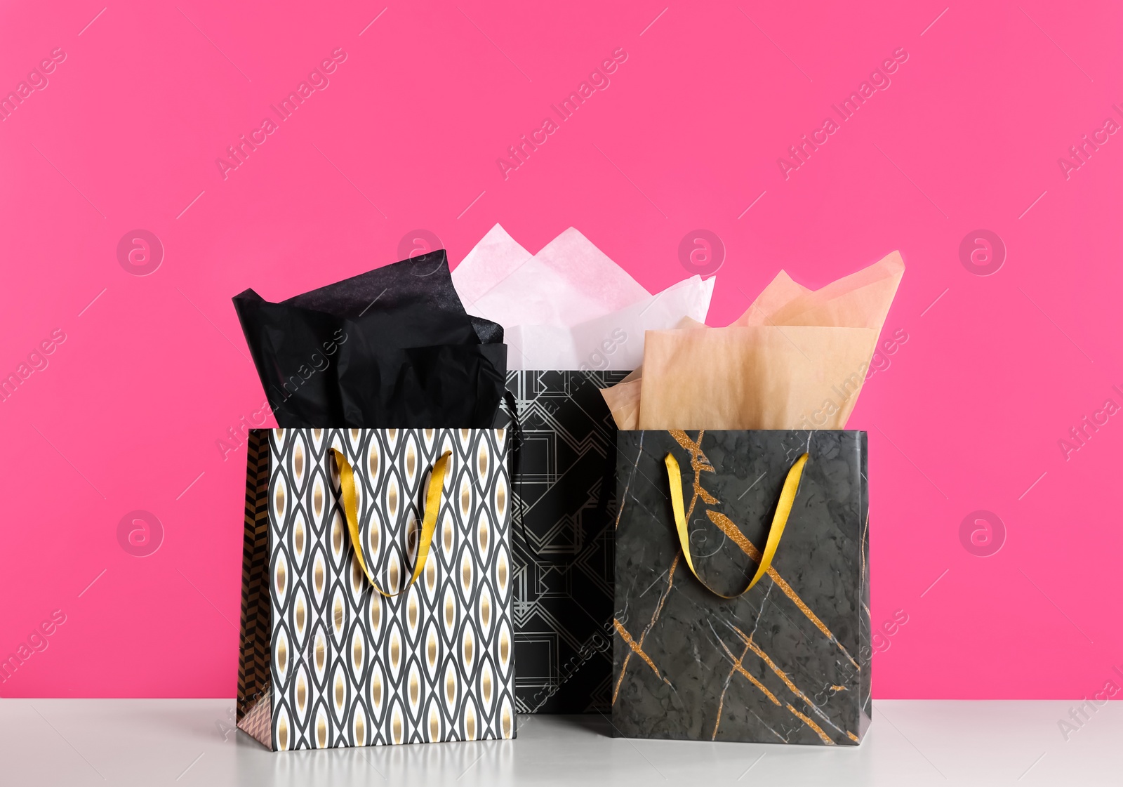 Photo of Gift bags with paper on white table against pink background