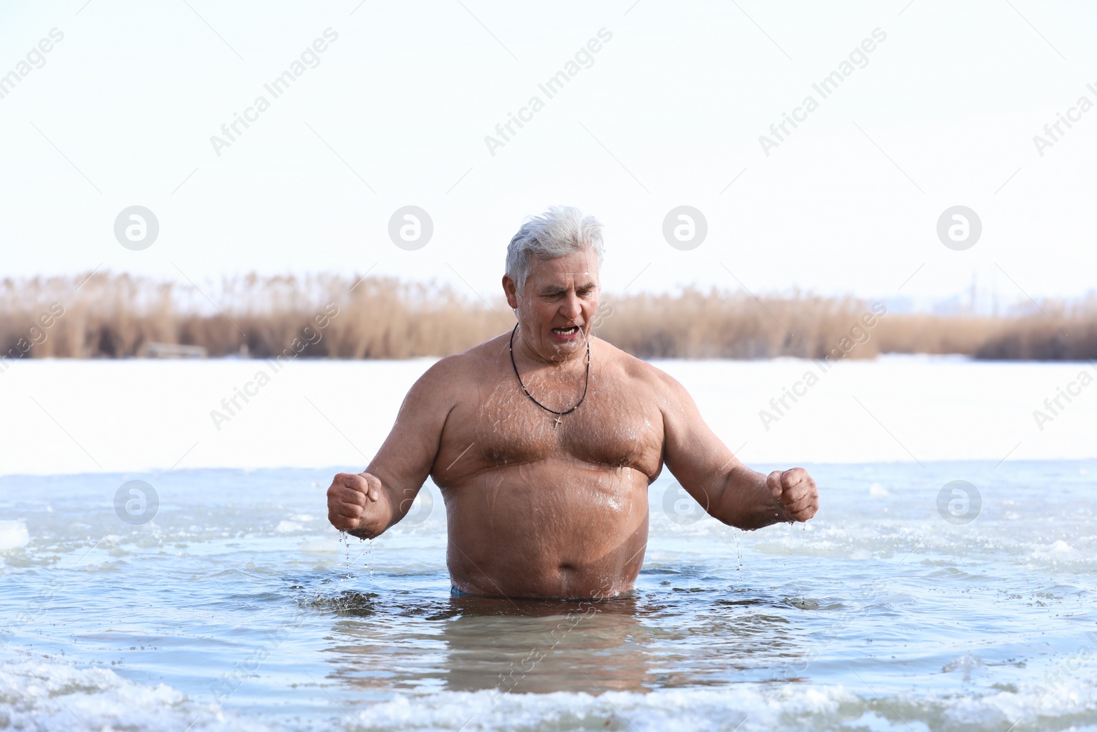 Photo of Mature man immersing in river on winter day. Baptism ritual