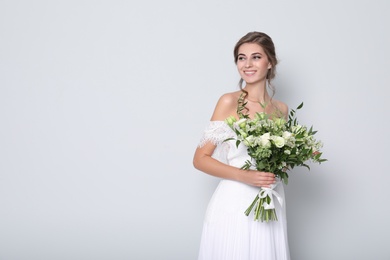 Young bride wearing wedding dress with beautiful bouquet on light grey background. Space for text