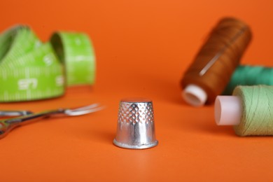 Photo of Thimble and different sewing tools on orange background