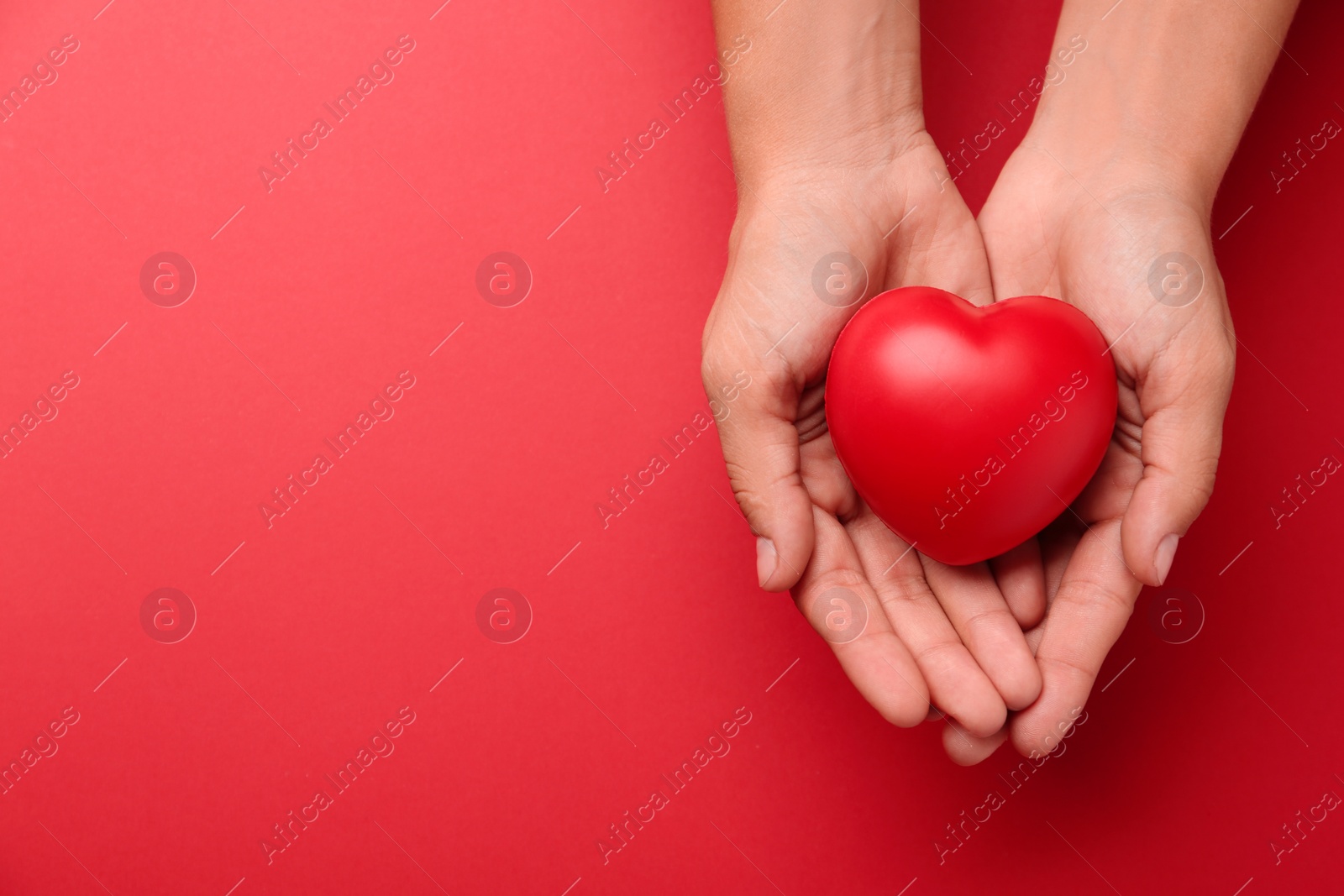 Photo of Woman holding decorative heart on red background, top view. Space for text