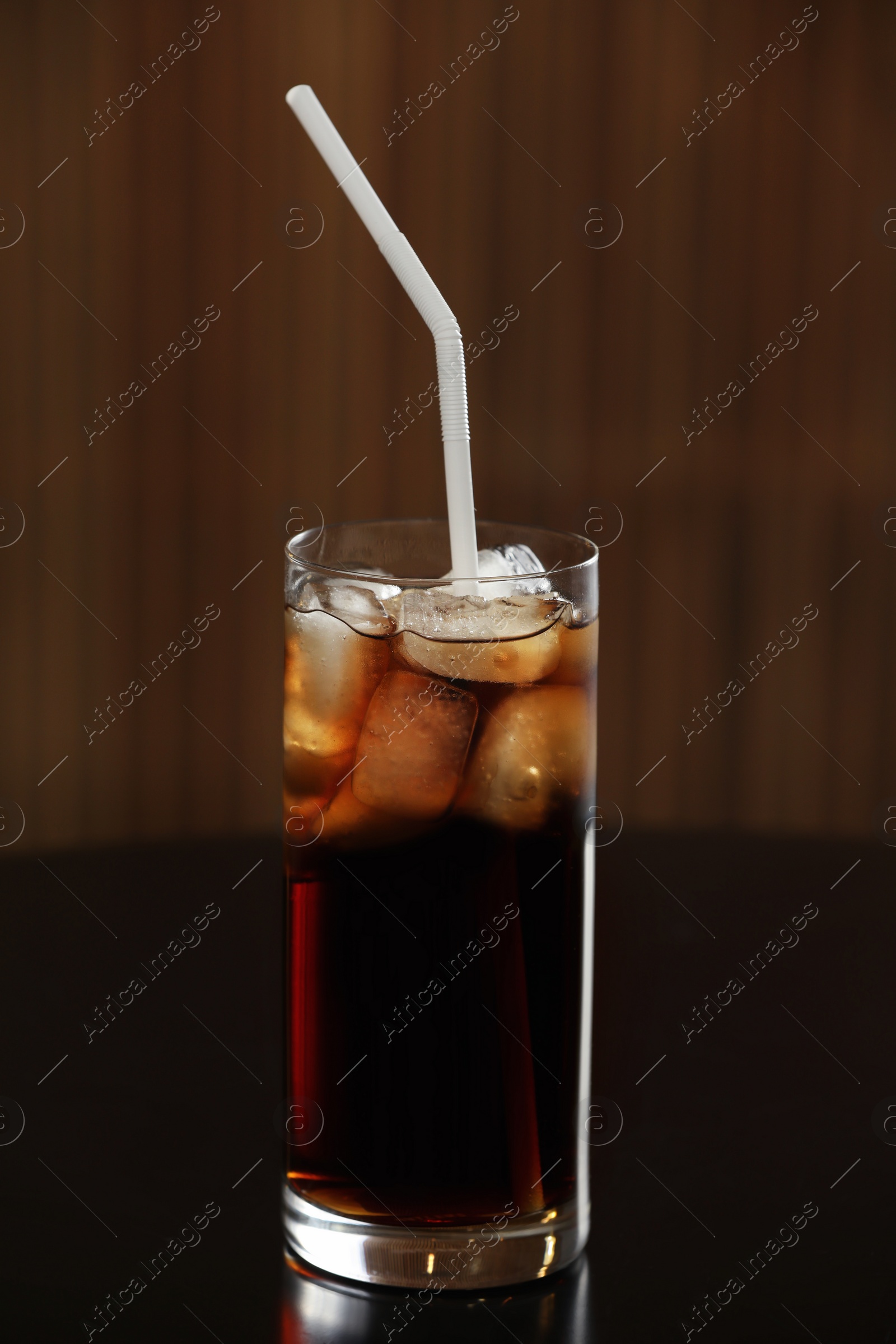 Photo of Glass of cola with ice on table against blurred background