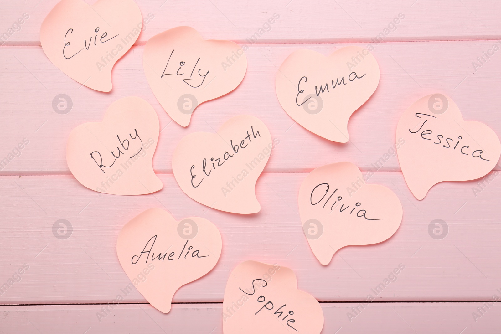 Photo of Paper stickers with different names on pink wooden background, flat lay. Choosing baby's name