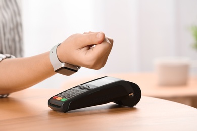 Photo of Woman using terminal for contactless payment with smart watch indoors