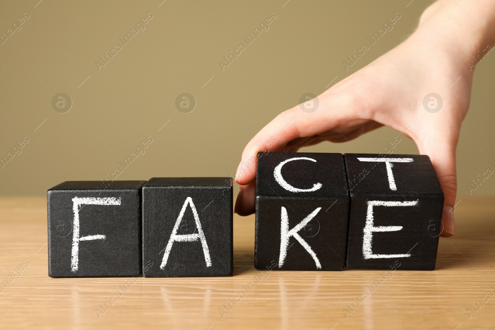 Photo of Woman making words FACT and FAKE with black cubes at wooden table, closeup