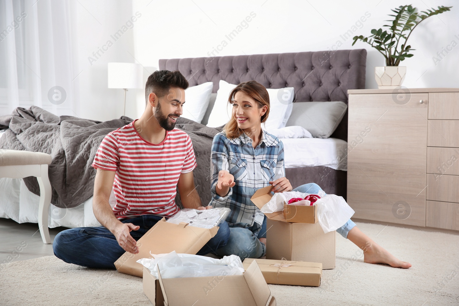 Photo of Young couple opening parcels in bedroom at home