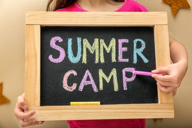 Girl writing SUMMER CAMP with colorful chalk on blackboard, closeup